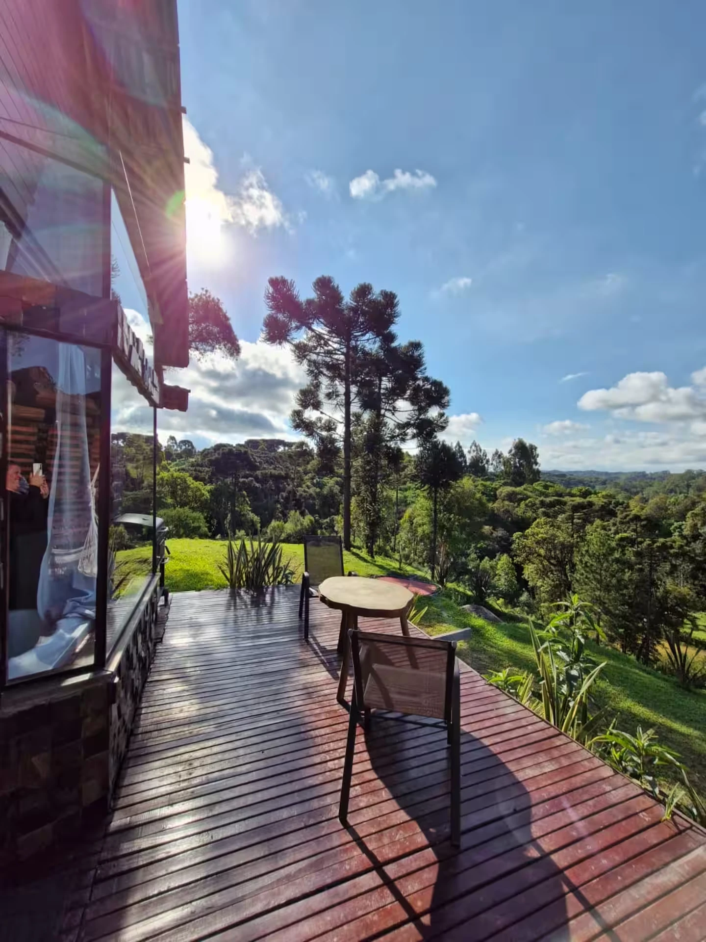 Deck de madeira com mesa e cadeiras, araucárias e céu azul