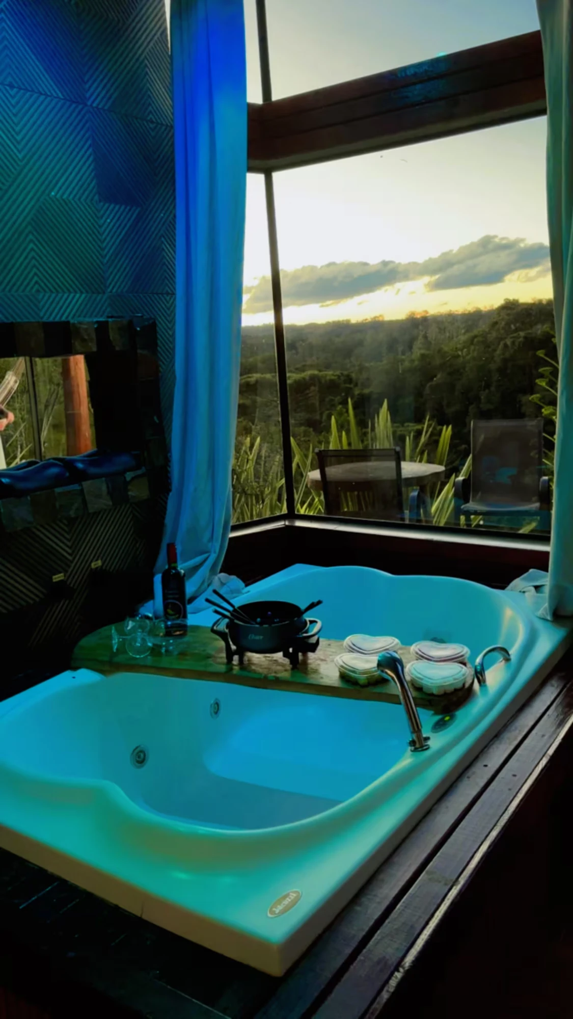 Hidromassagem ao entardecer, com tábua de fondue, vinho e taças apoiados na borda
