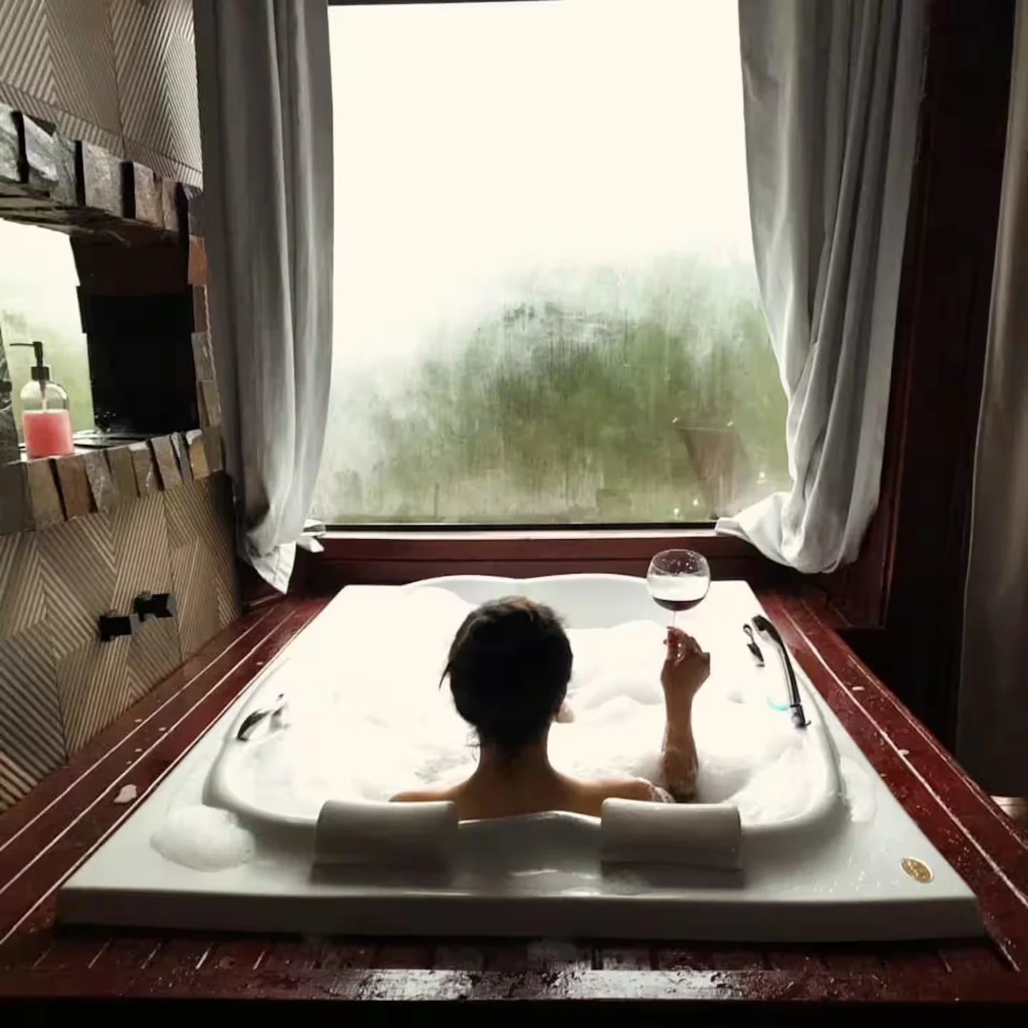 Hóspede na hidromassagem segurando uma taça de vinho, com a janela embaçada pela neblina